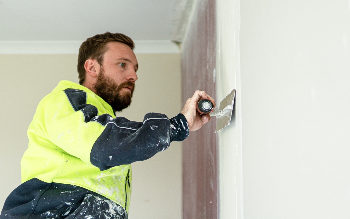 Man in high visibility wear plastering a wall in a residential home