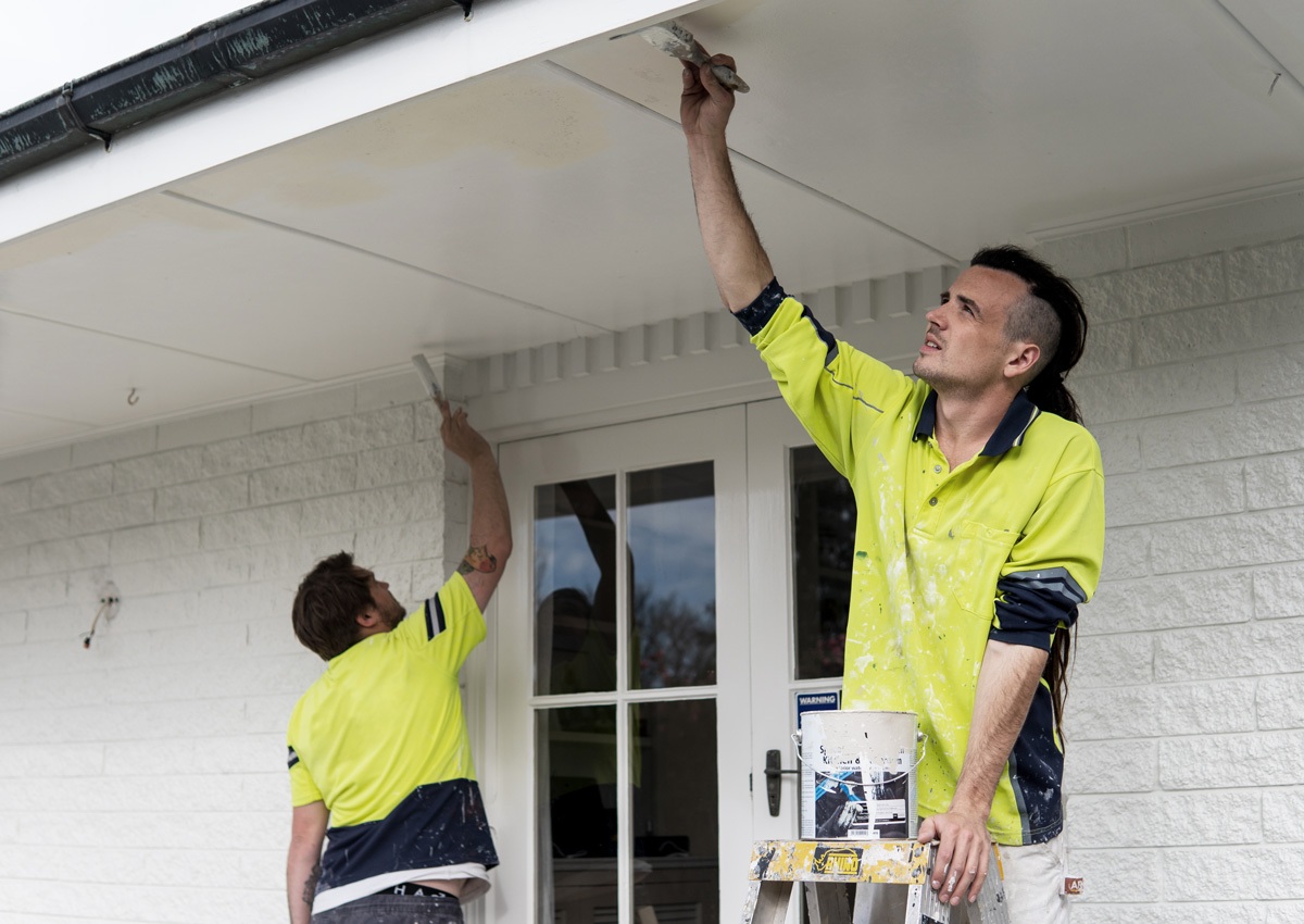 Two men painting the exterior of a residential brick home - Painting services